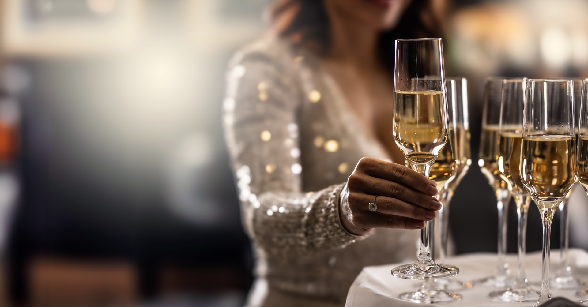 A bartender holds a plate with pink champagne and a woman in a cocktail dress takes one of the glasses at an event, party or wedding.