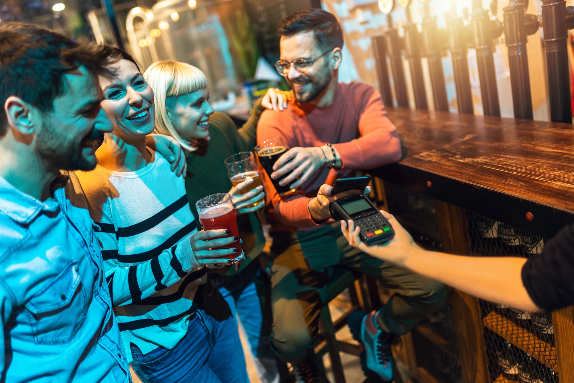 Diverse friends in bar paying with cellular device